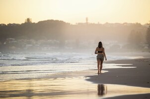 A person walking on a beach with a sunset in the background.