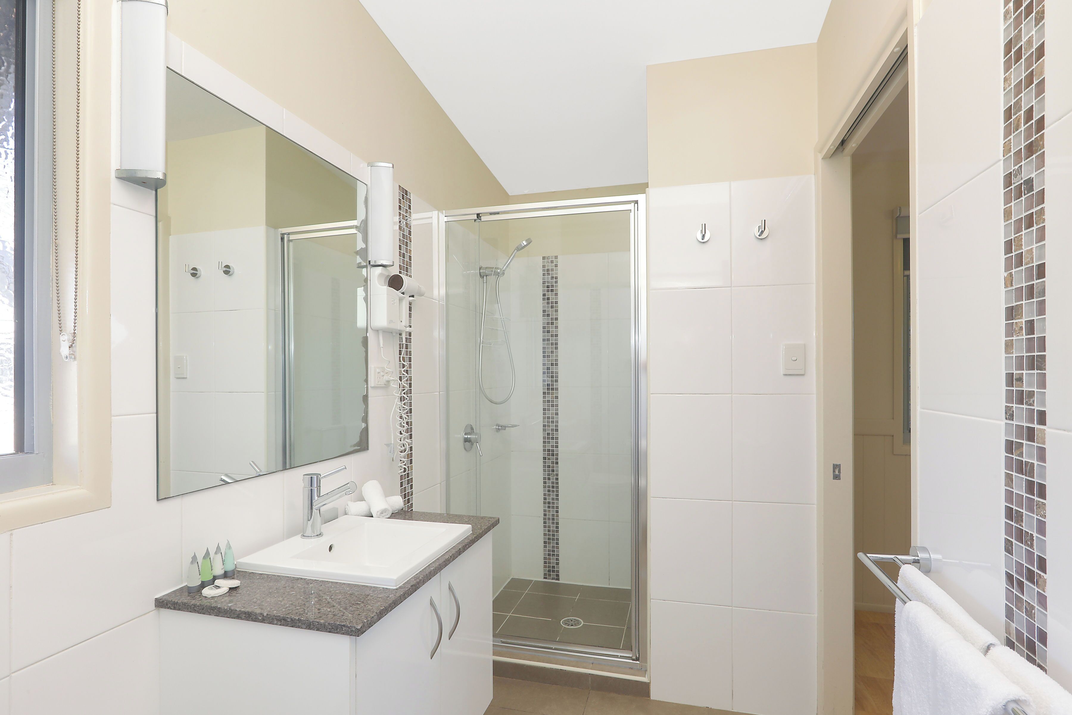 A modern bathroom with a glass-enclosed shower, a large mirror, and a granite countertop.