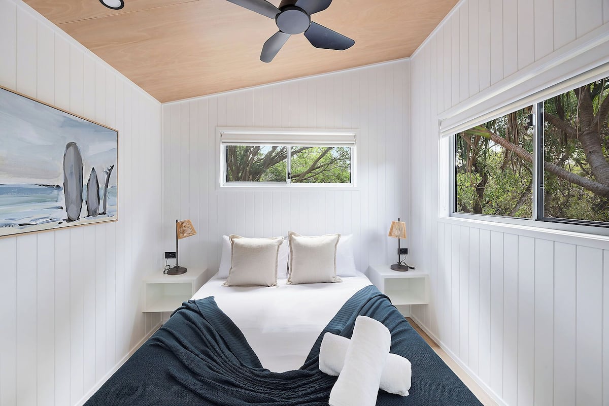 Quarto com cama, ventoinha no teto, janela, quadro e abajures.
