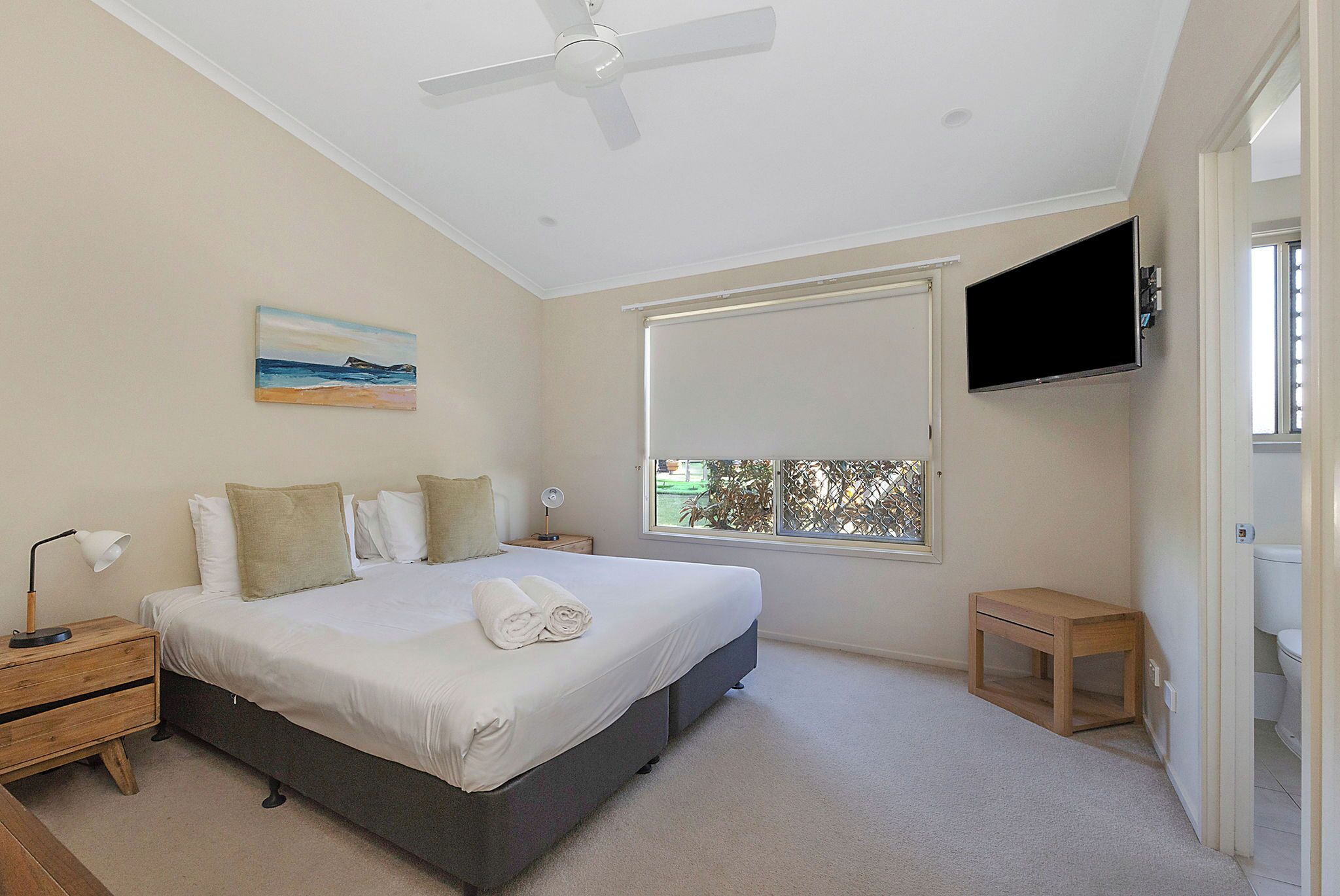 Une chambre à coucher comprenant un lit, une table de chevet, une commode, un ventilateur de plafond, une fenêtre avec vue et un téléviseur fixé au mur.