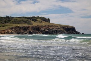 A coastal landscape with a rocky cliff and waves crashing onto the shore.