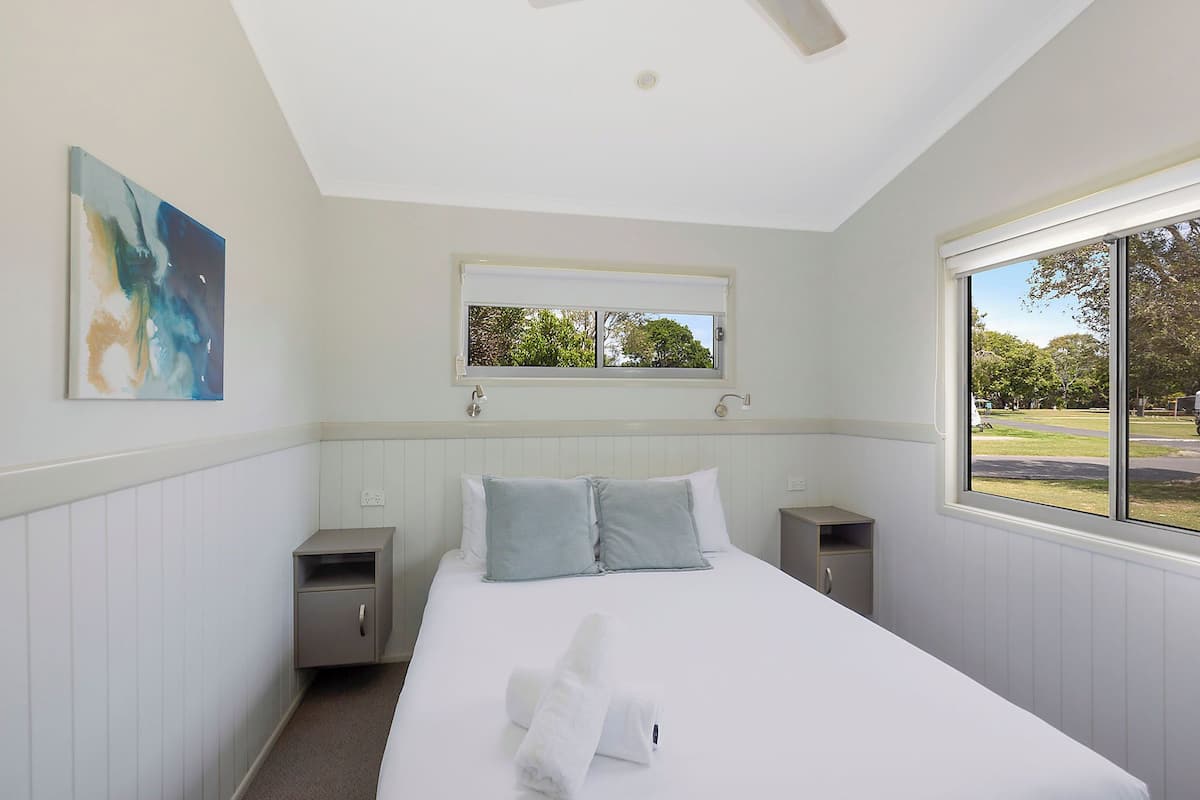 Quarto com cama, janela, um quadro e vista para o exterior.