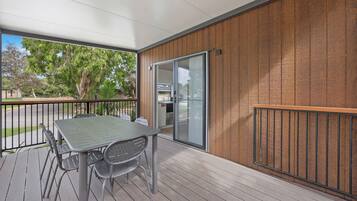 Un espace extérieur abrité, doté d’une table et de chaises, d’une porte-fenêtre coulissante et d’un mur en bois.
