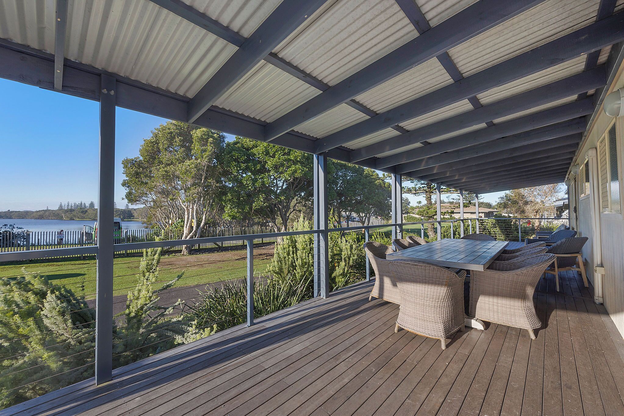 A covered outdoor area with a table and chairs, overlooking a body of water and greenery.