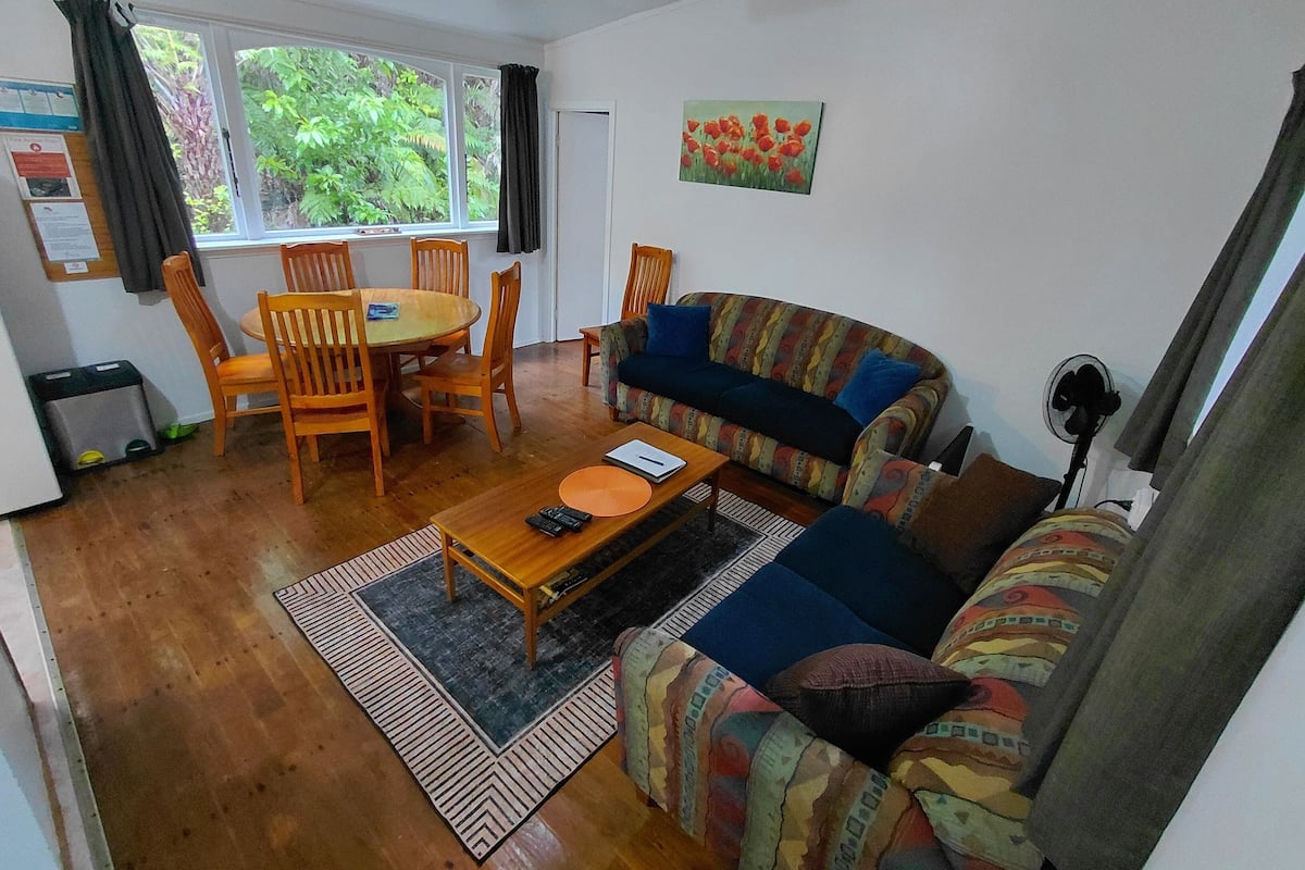 A living room with a sofa, a coffee table, a dining table with chairs, and a window with curtains.