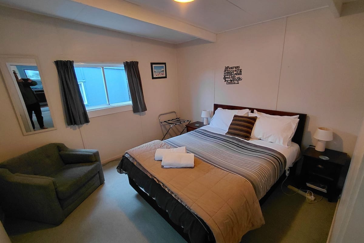 A hotel room with a bed, a chair, a window, a wall decoration, and a nightstand.