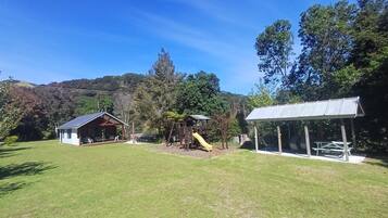 Enjoy a serene outdoor setting with a lawn, playhouse, and picnic area amidst a natural landscape.