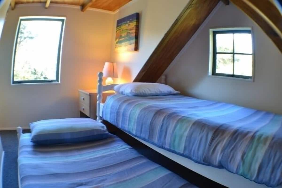 A bedroom with two single beds, a nightstand, a lamp, and two windows.