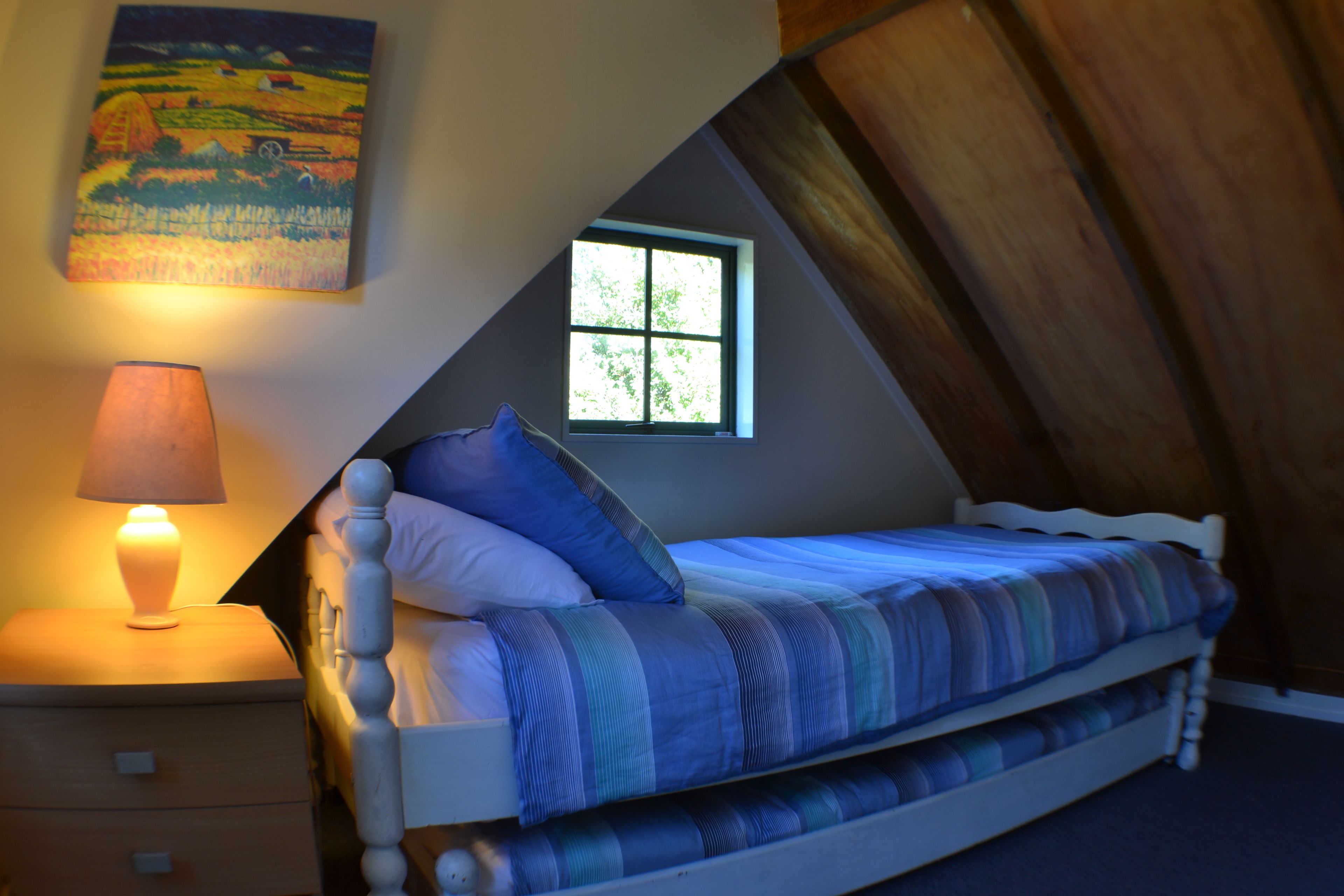 A bedroom with a bed, a nightstand, a lamp, a window, and a painting on the wall.