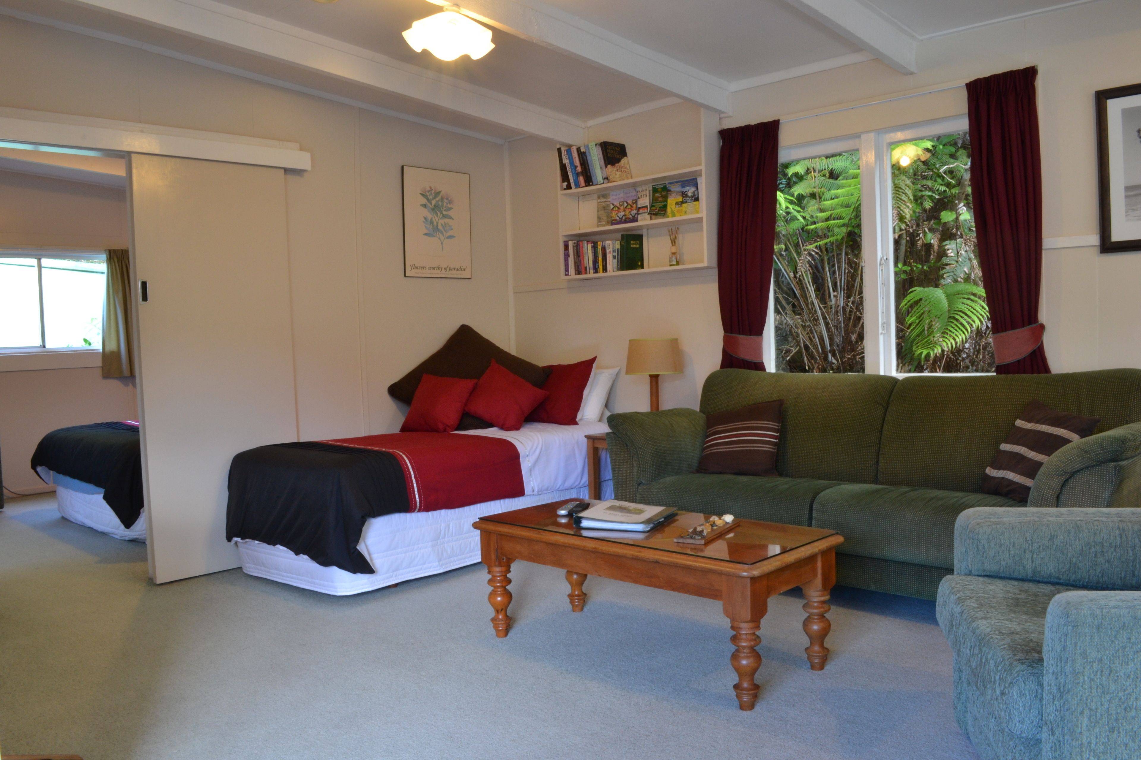 A cozy living room with a bed, a green sofa, a wooden coffee table, and a bookshelf.
