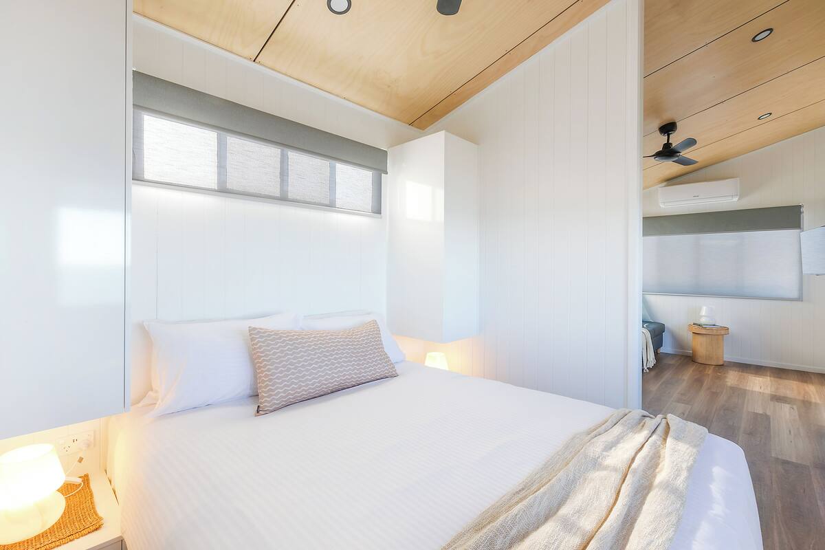 A modern bedroom with a large bed, bedside lamp, and a ceiling fan.