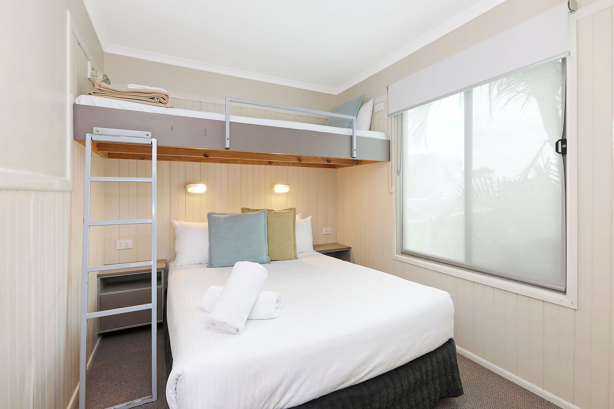 A single bed with a bunk above, a ladder, bedside tables, and a large window.