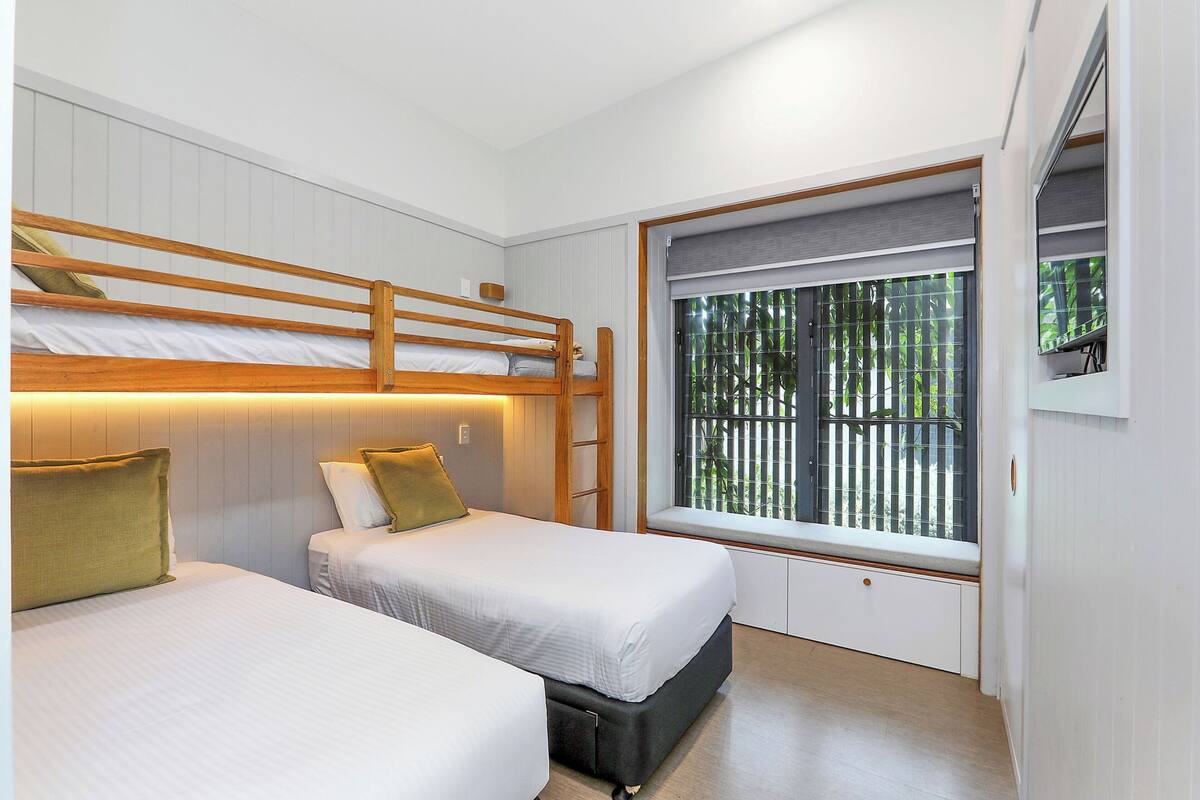 A room with two beds, a window with a view of greenery, and a built-in bench.