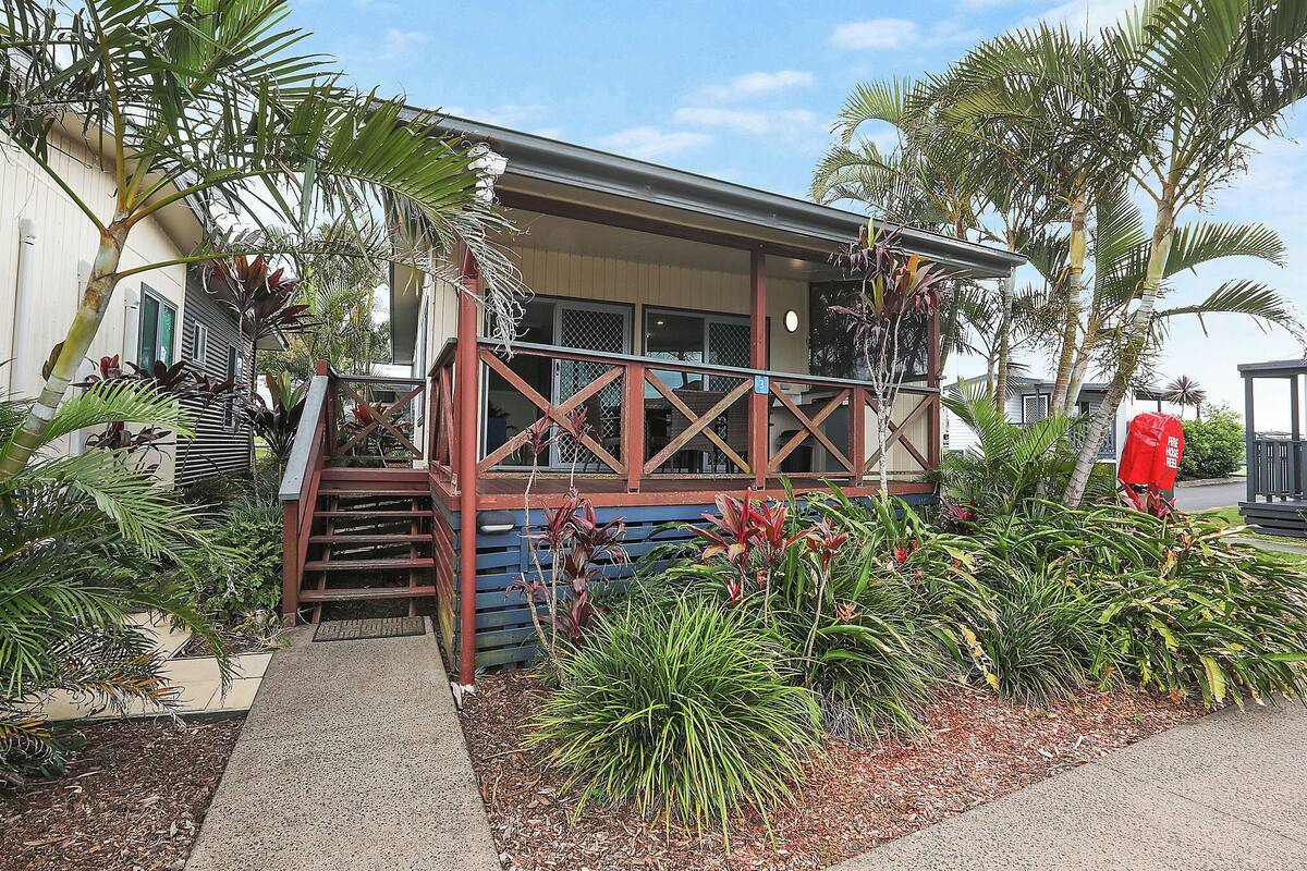 A building with a covered porch, steps leading to a door, and various tropical plants.