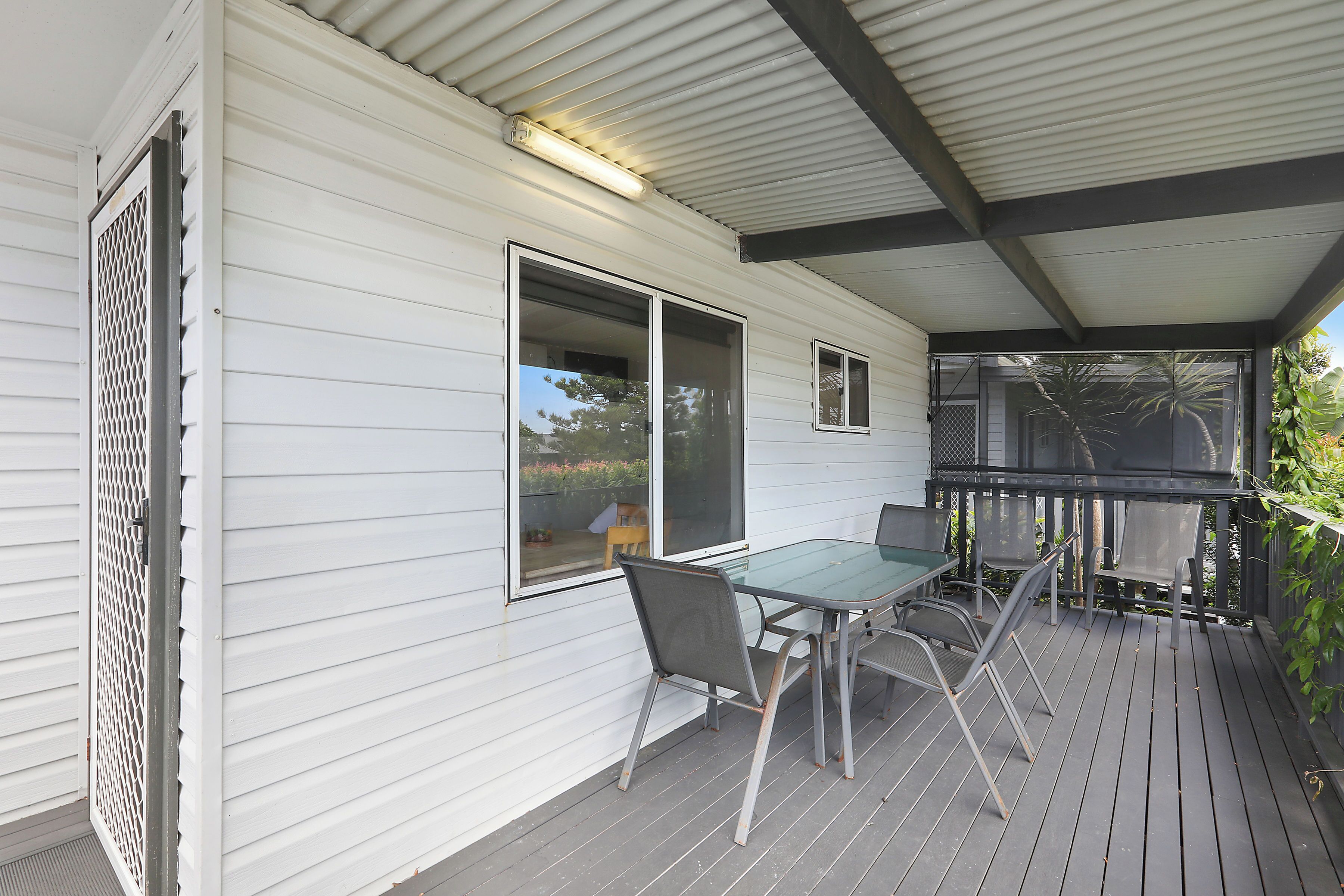 A covered outdoor area with a table and chairs, a window, and a door with a metal screen.