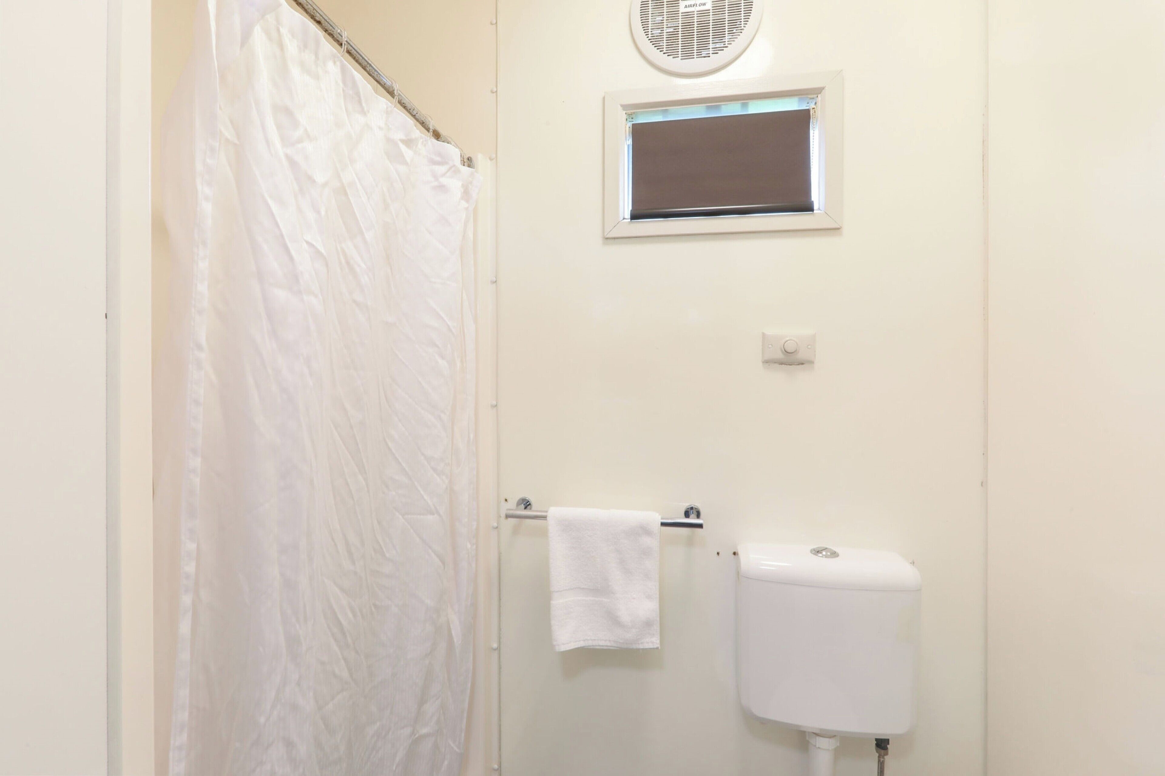 A bathroom with a white toilet, a towel hanging on a rack, a window, and a shower curtain.
