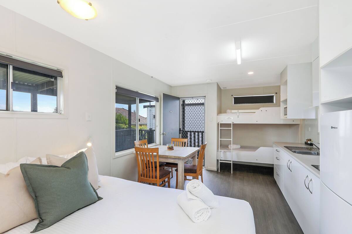 A compact hotel room with a bed, a small dining table, and a kitchenette.