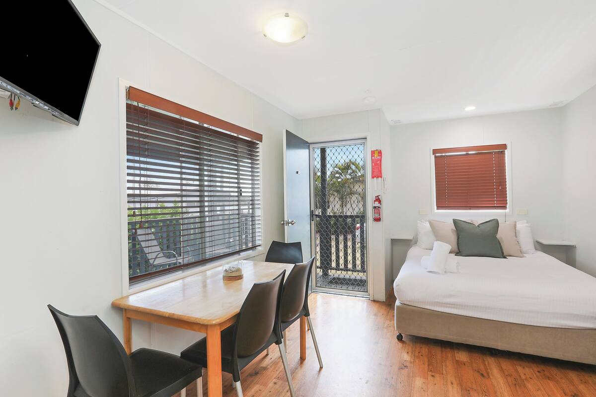 A bedroom with a bed, bedside table, and a window with blinds.