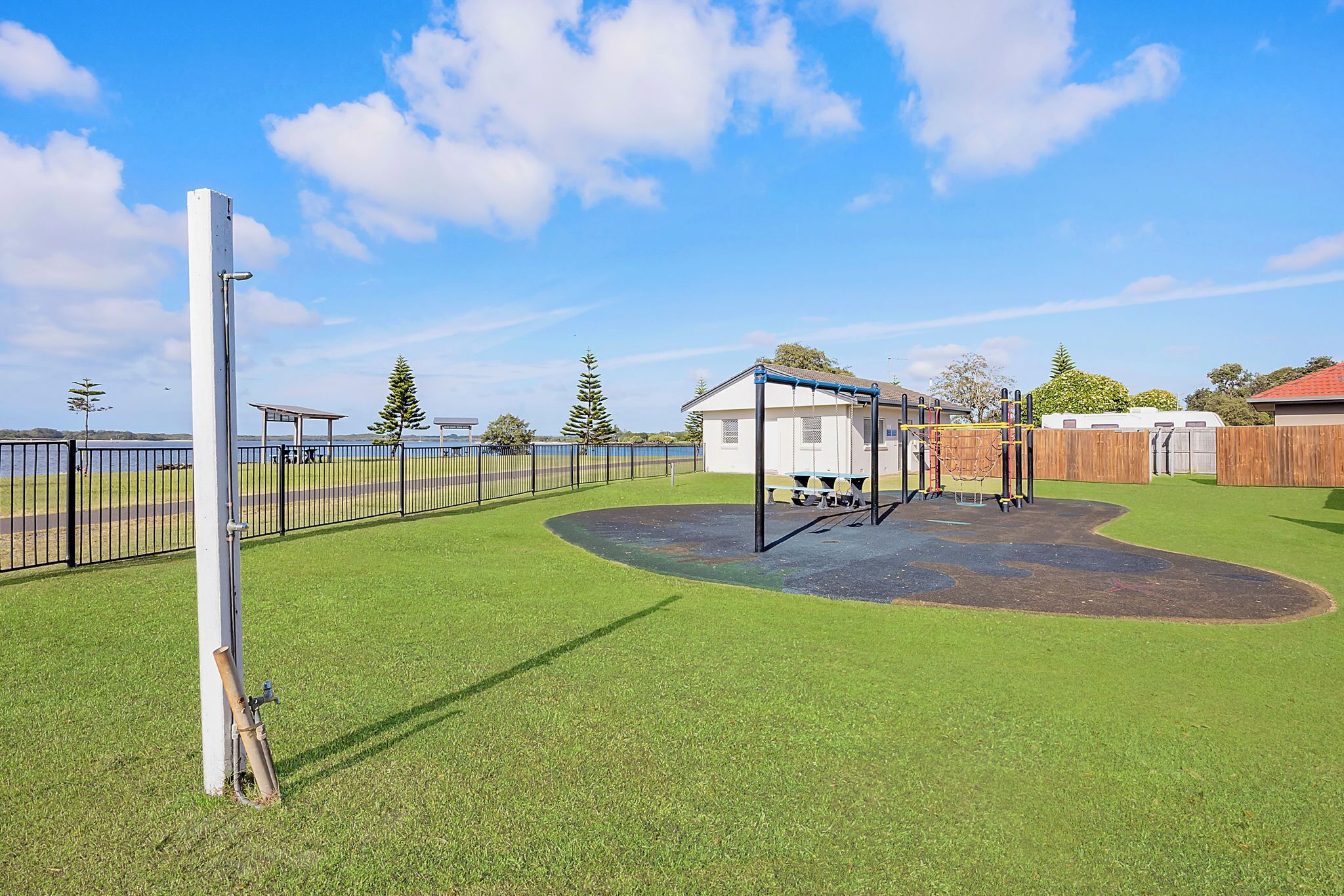 A playground with a swing set and a slide, surrounded by a fenced area with a house and a wooden fence in the background.