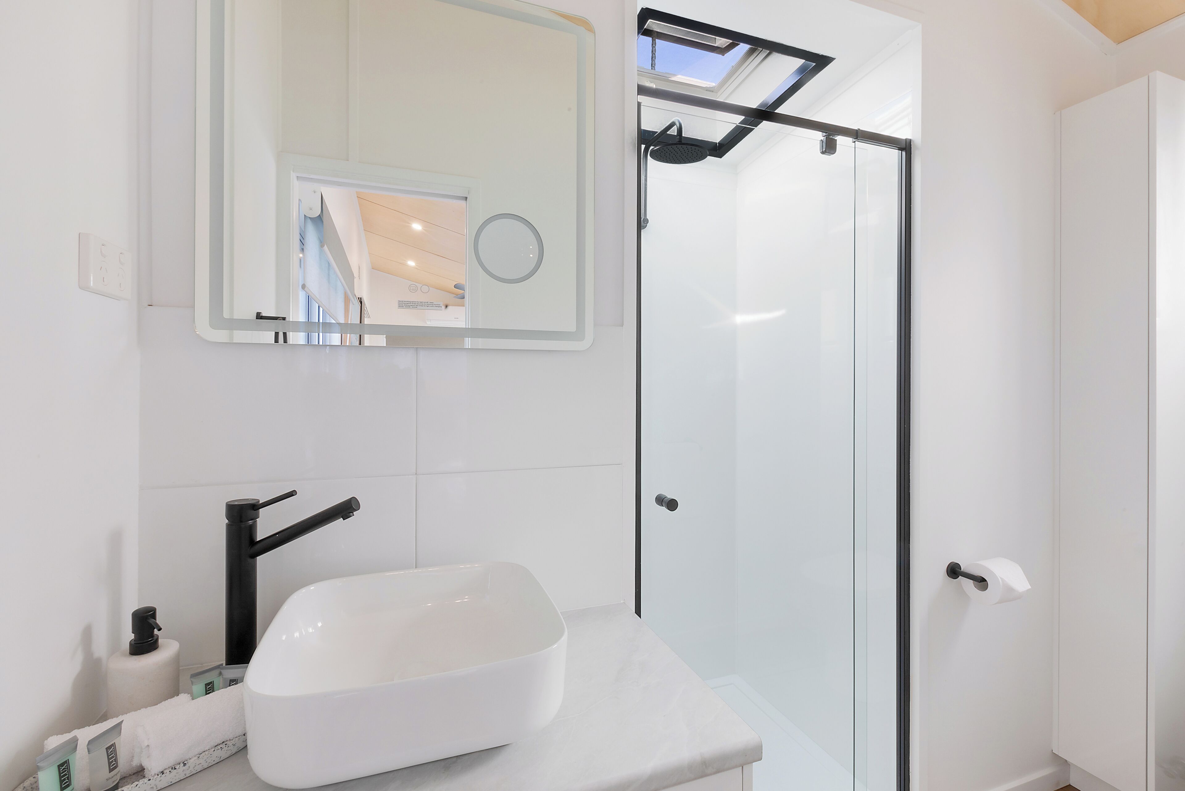 Un baño moderno con lavamanos blanco, espejo y cabina de ducha de vidrio.
