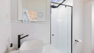 Un baño moderno con lavamanos blanco, espejo y cabina de ducha de vidrio.