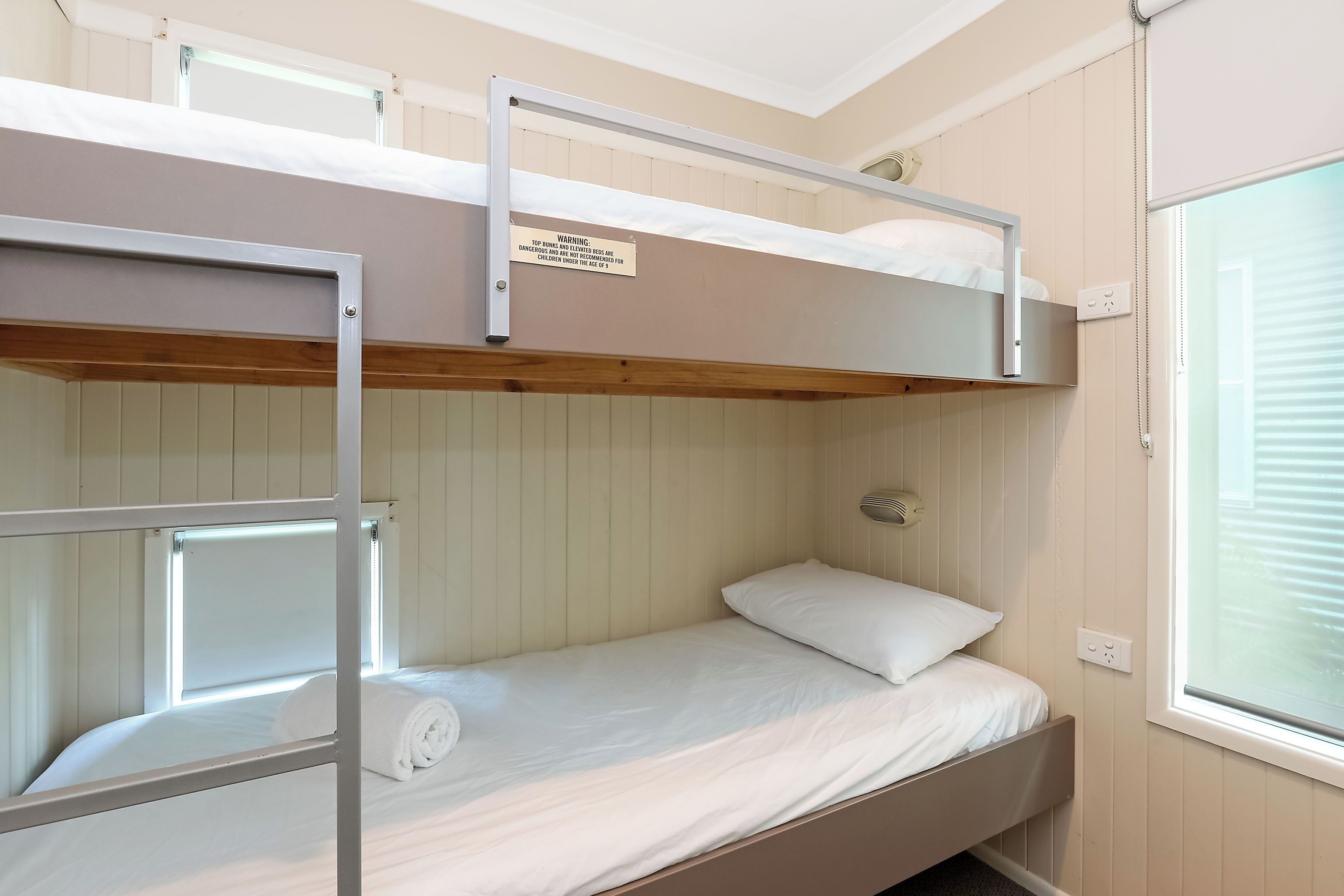 A bunk bed room with a warning sign, a window, and a power outlet.