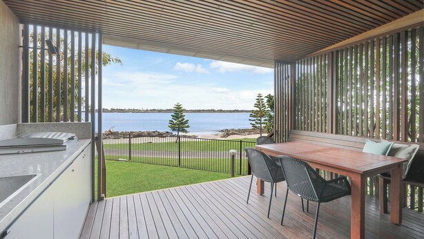 A balcony with a wooden deck, a table with chairs, and a view of the sea. - Reflections Shaws Bay - Holiday Park (East Ballina)
