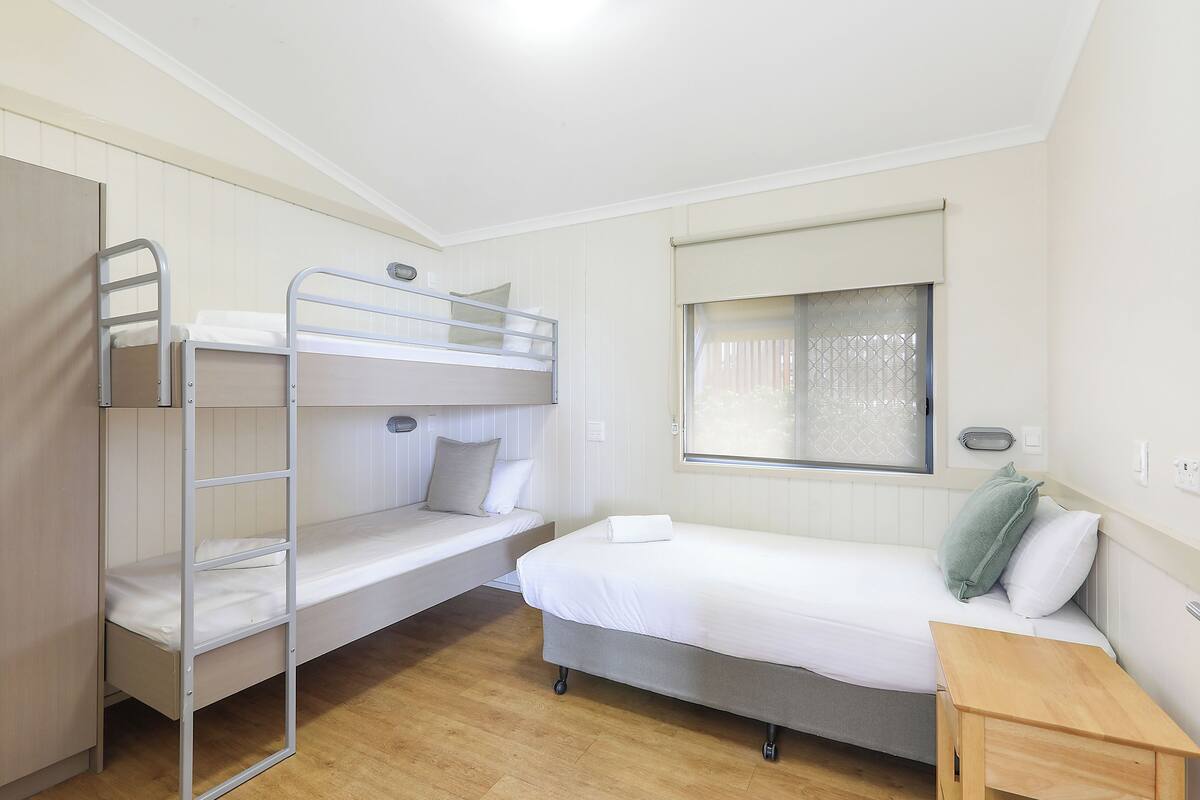 A bunk bed room with a single bed and a small wooden table.