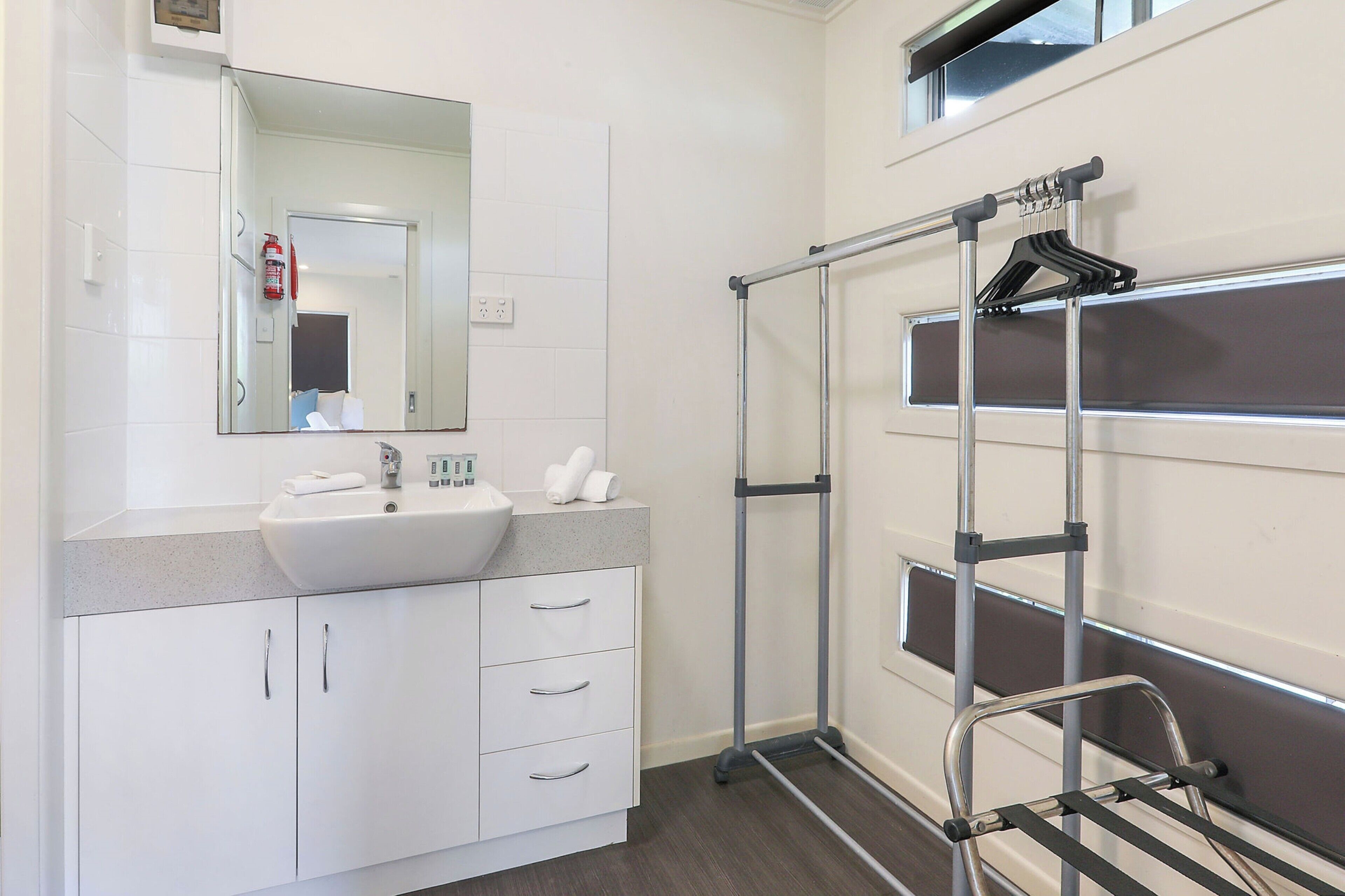 Un baño moderno con un lavamanos blanco, espejo y un perchero metálico.