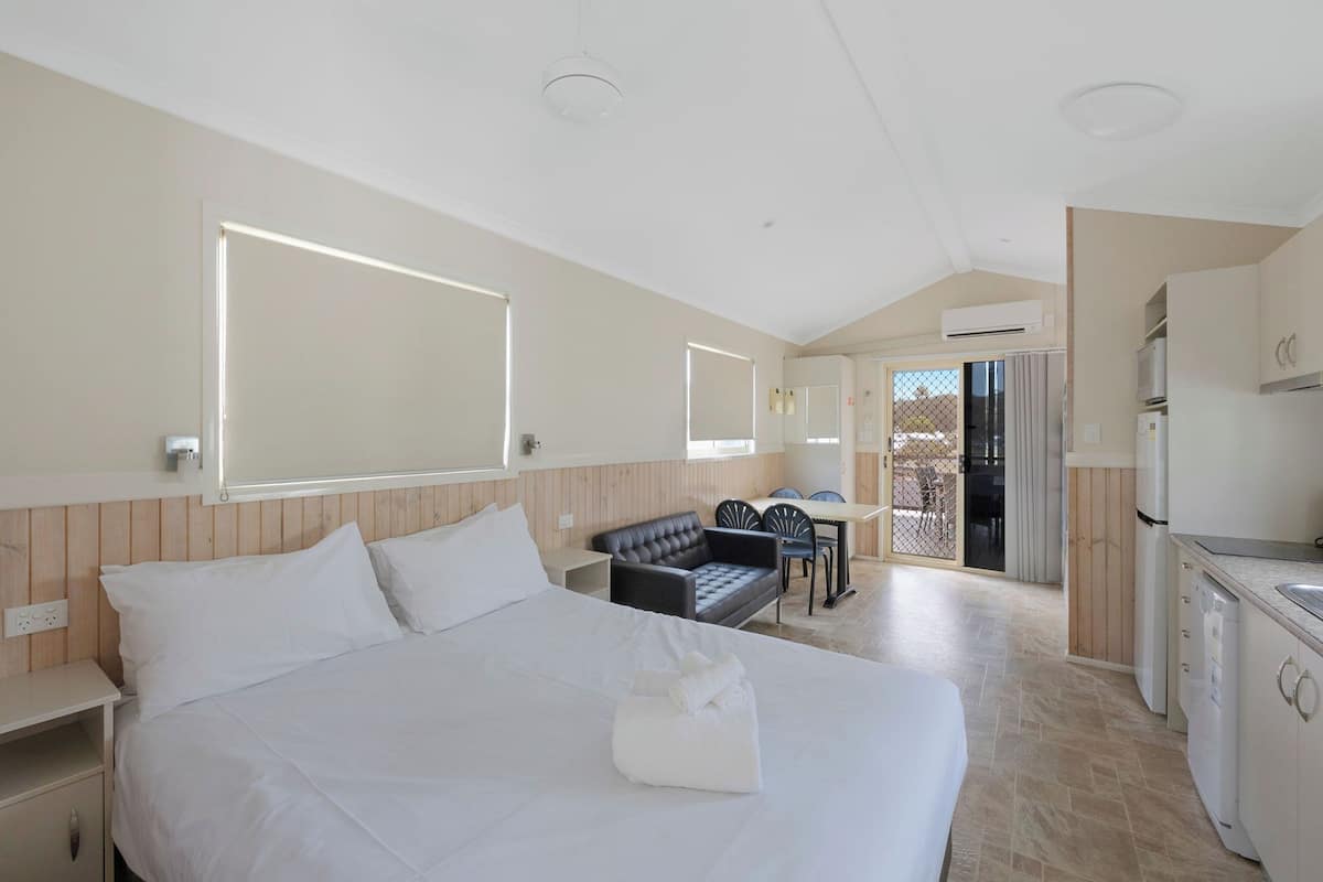 A hotel room with a large bed, a small dining area, and a kitchenette.