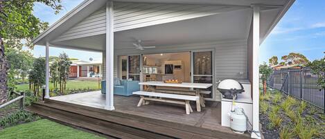 A covered outdoor patio with a wooden deck, a table, and a bench.