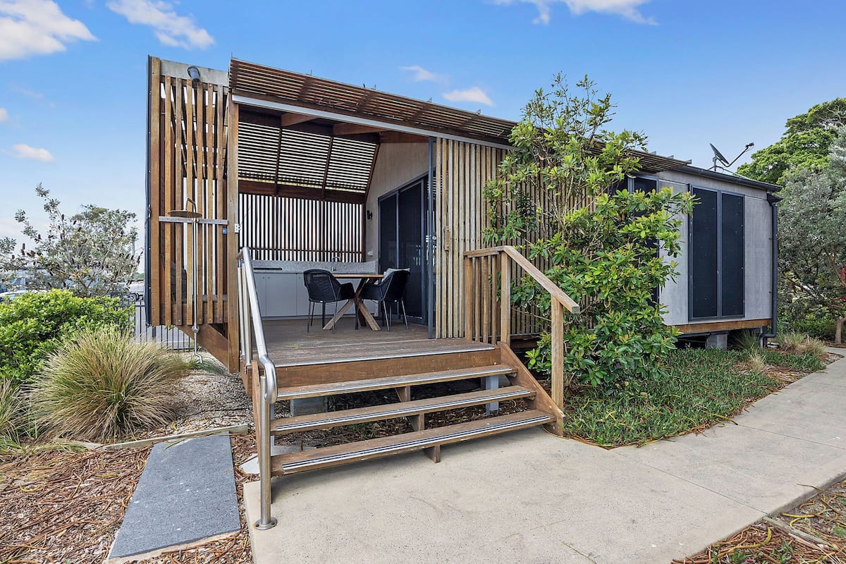 A modern house with a wooden deck, a dining area with chairs, and a staircase leading to the entrance.