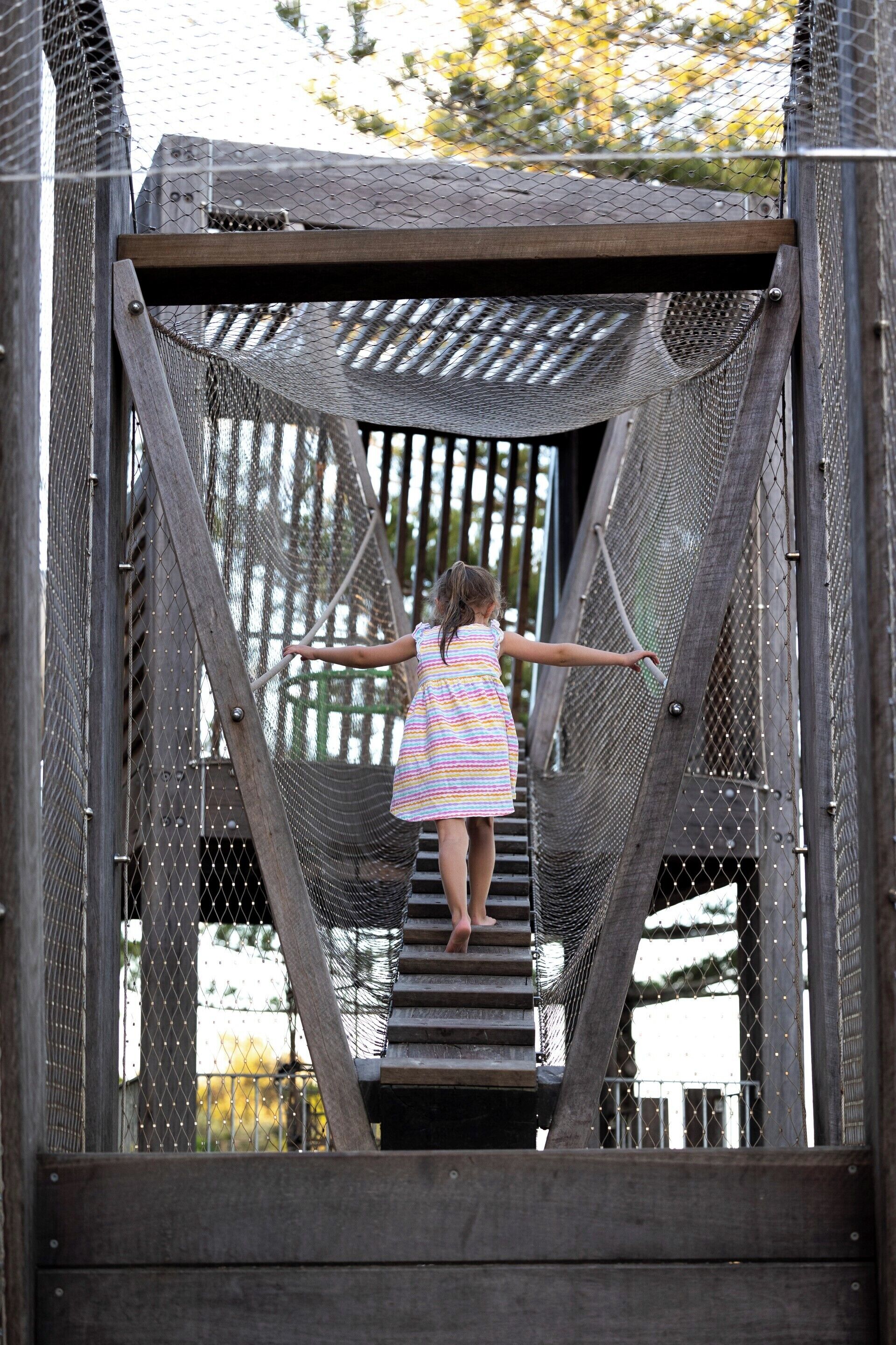 A person standing on a wooden bridge with a mesh walkway, surrounded by metal railings.