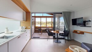 A modern kitchen with a large window, a dining area with a table and chairs, and a flat-screen TV mounted on the wall. - Reflections Evans Head - Holiday Park (Evans Head)