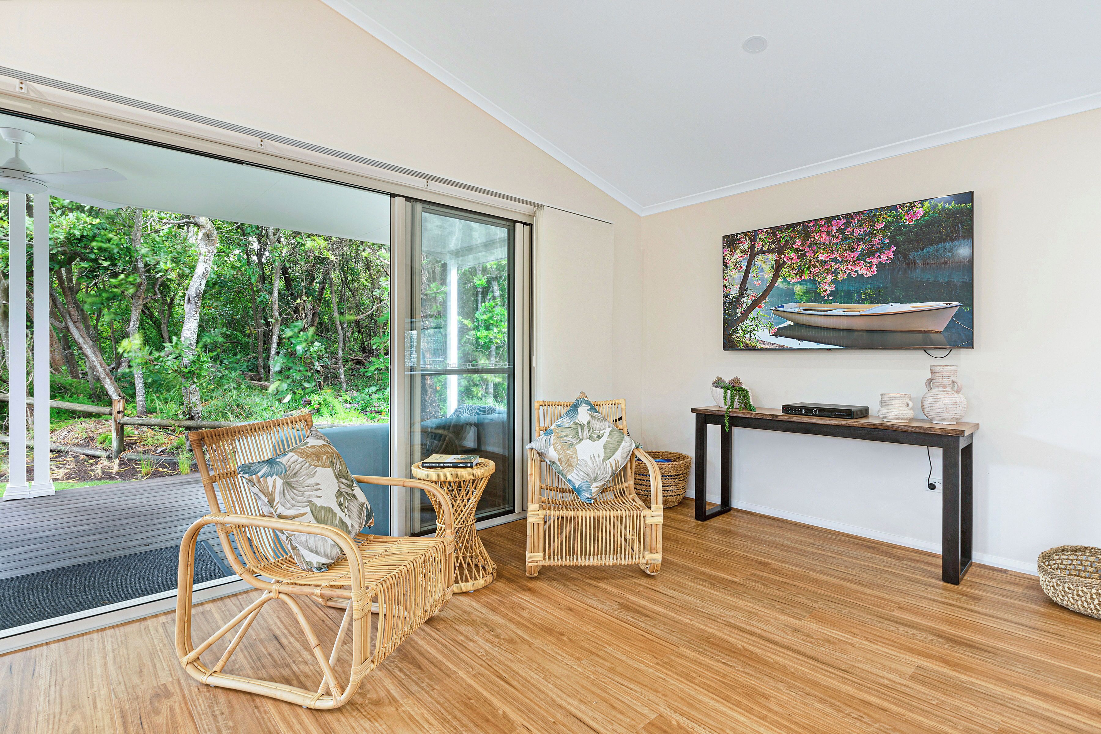 A room with wicker furniture, a wooden floor, a glass door leading to a garden, and a painting on the wall.