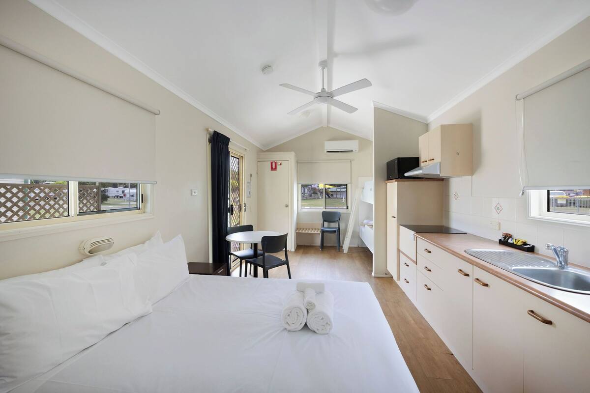 A hotel room with a bed, a small table, two chairs, a kitchenette, and a window with a view.