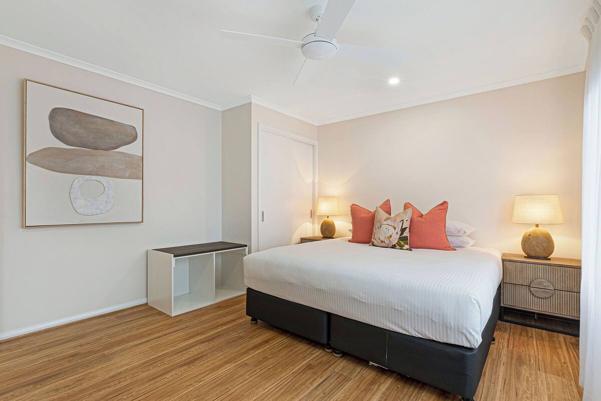 A bedroom with a bed, bedside tables, a ceiling fan, and a wall-mounted artwork.