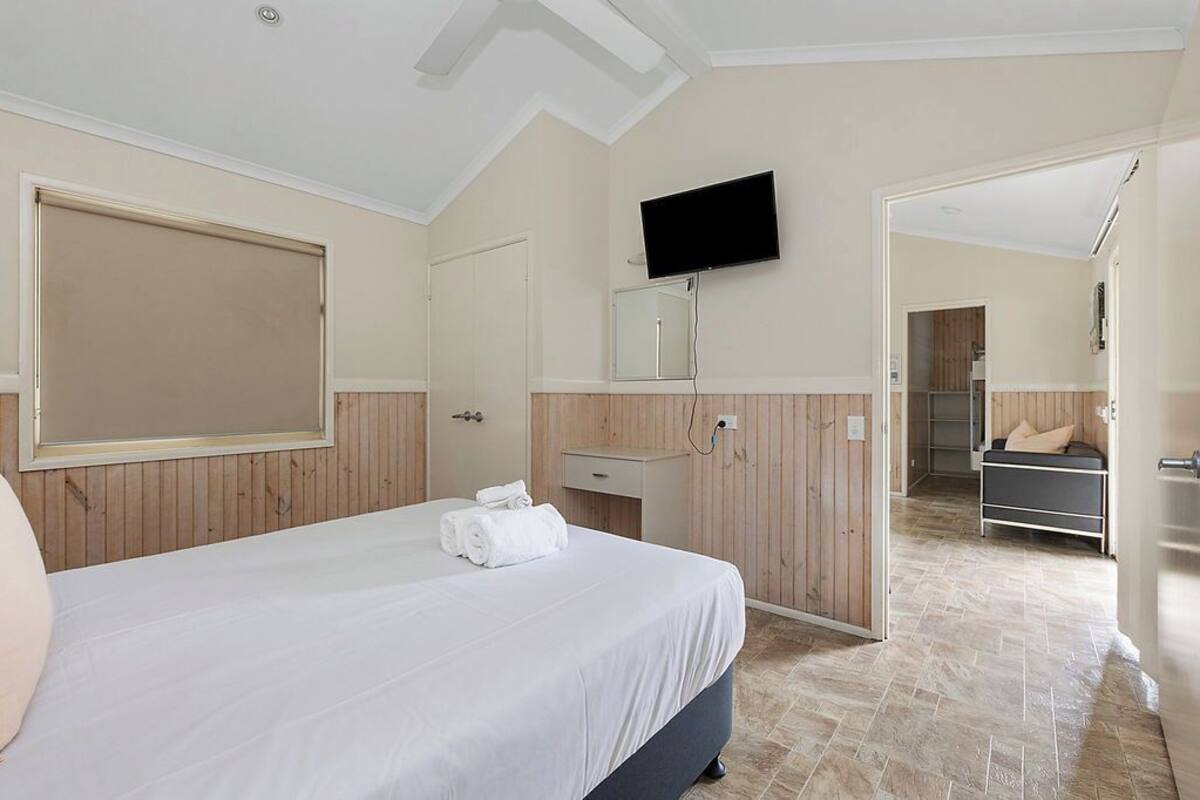 A bedroom with a bed, a TV mounted on the wall, a mirror, and a bathroom visible through an open door.