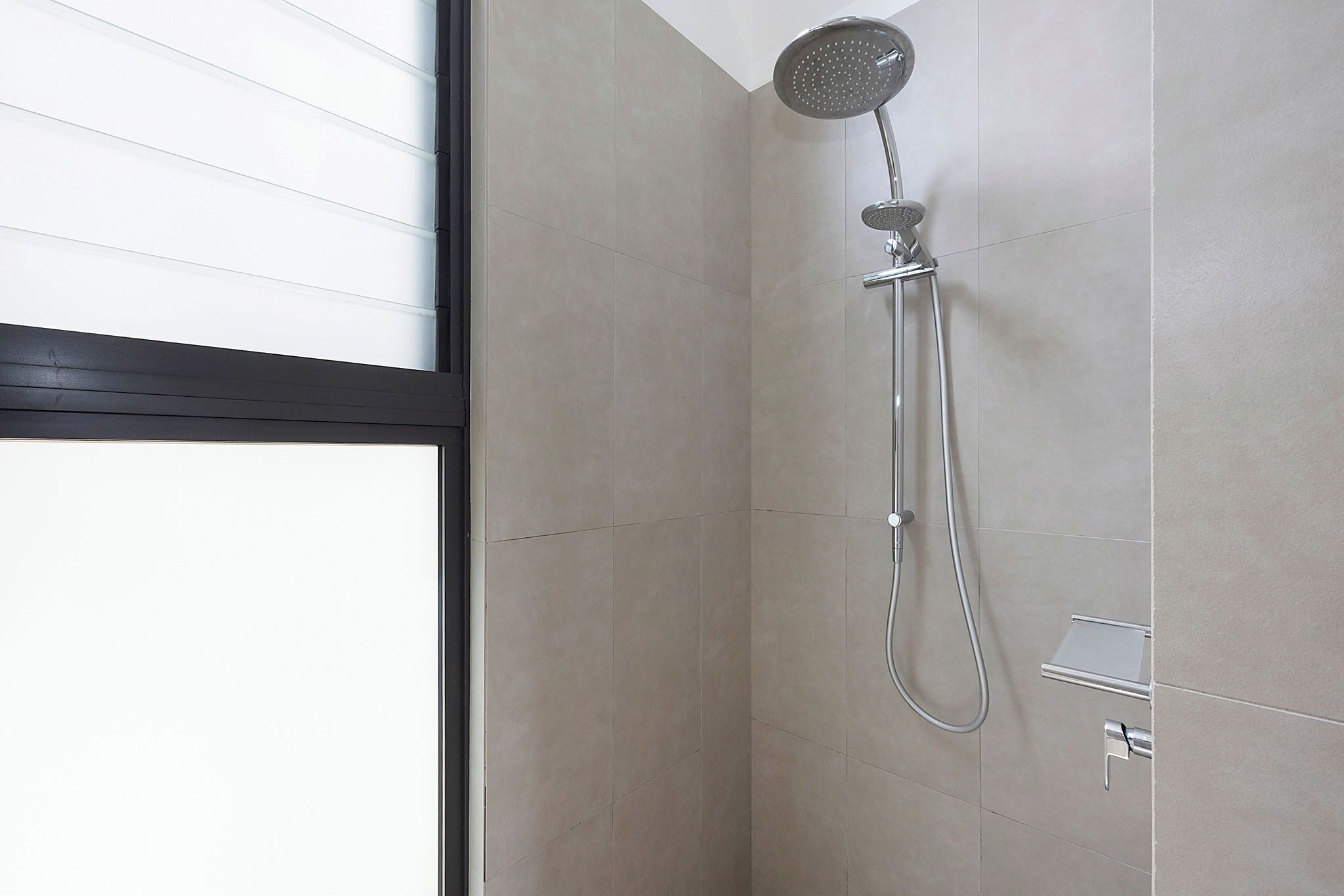 Een moderne douche met een handdouche en een bedieningspaneel aan de muur.