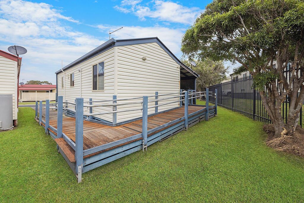 A single-story, white mobile home with a wooden deck and a metal fence.