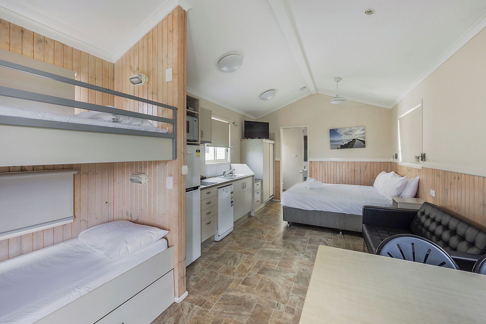 A compact hotel room with bunk beds, a kitchenette, a dining area, and a single bed.