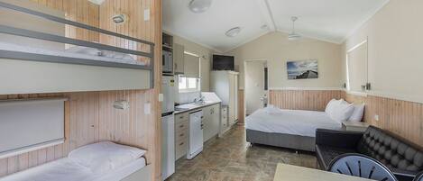 A compact hotel room with bunk beds, a kitchenette, a dining area, and a single bed.