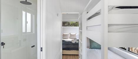 Une chambre d’hôtel moderne dotée d’une douche à parois de verre, d’un lit avec une tête de lit sombre et d’une vue sur les arbres par la fenêtre.