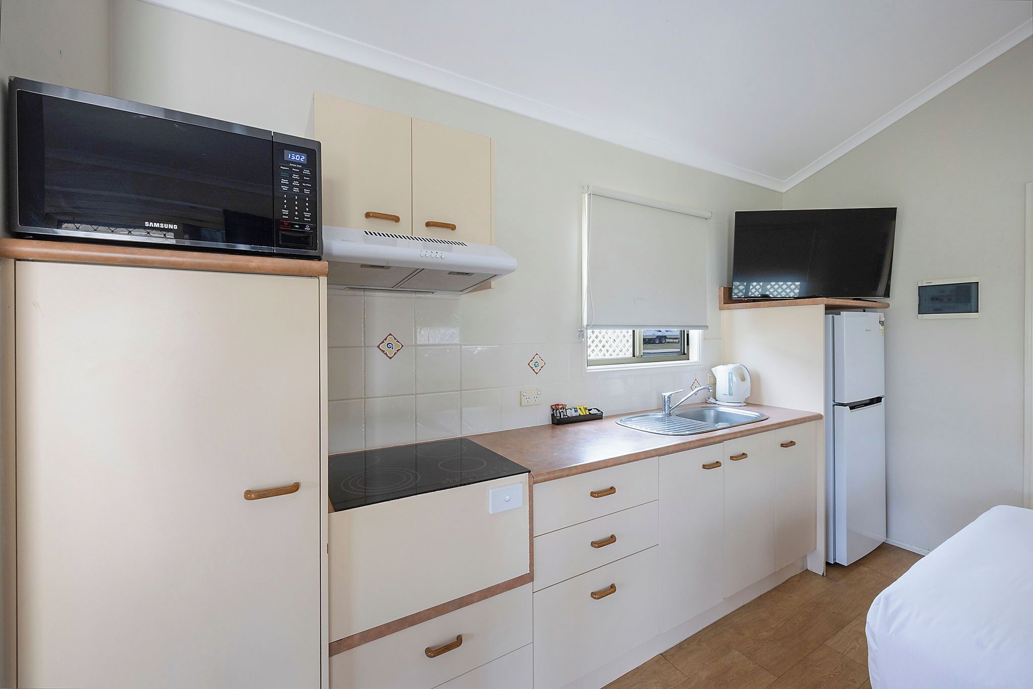 A compact kitchen with a microwave, stove, sink, and a small refrigerator.