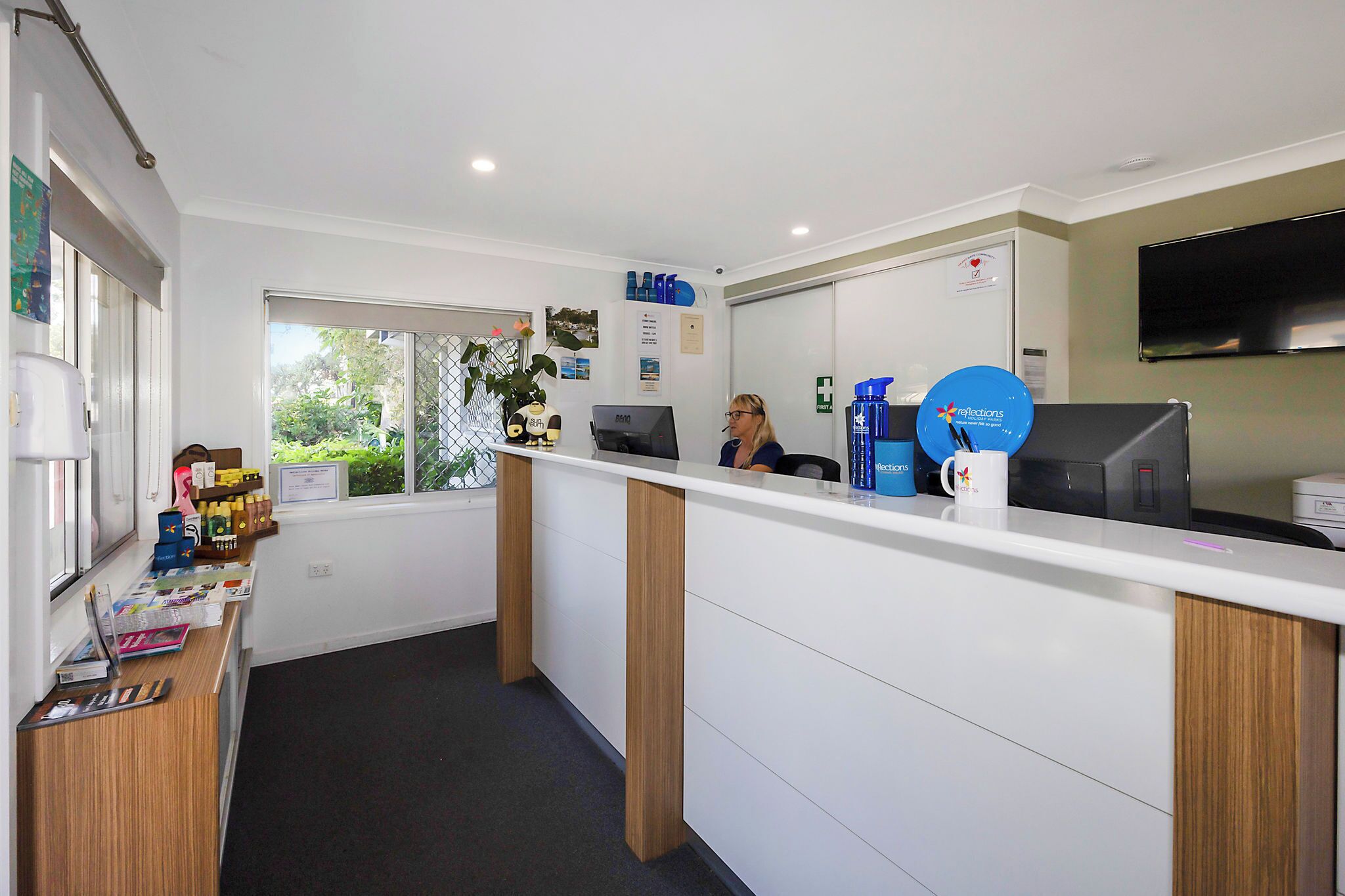 A reception area with a white counter, wooden accents, a computer, and a window with a view of greenery.