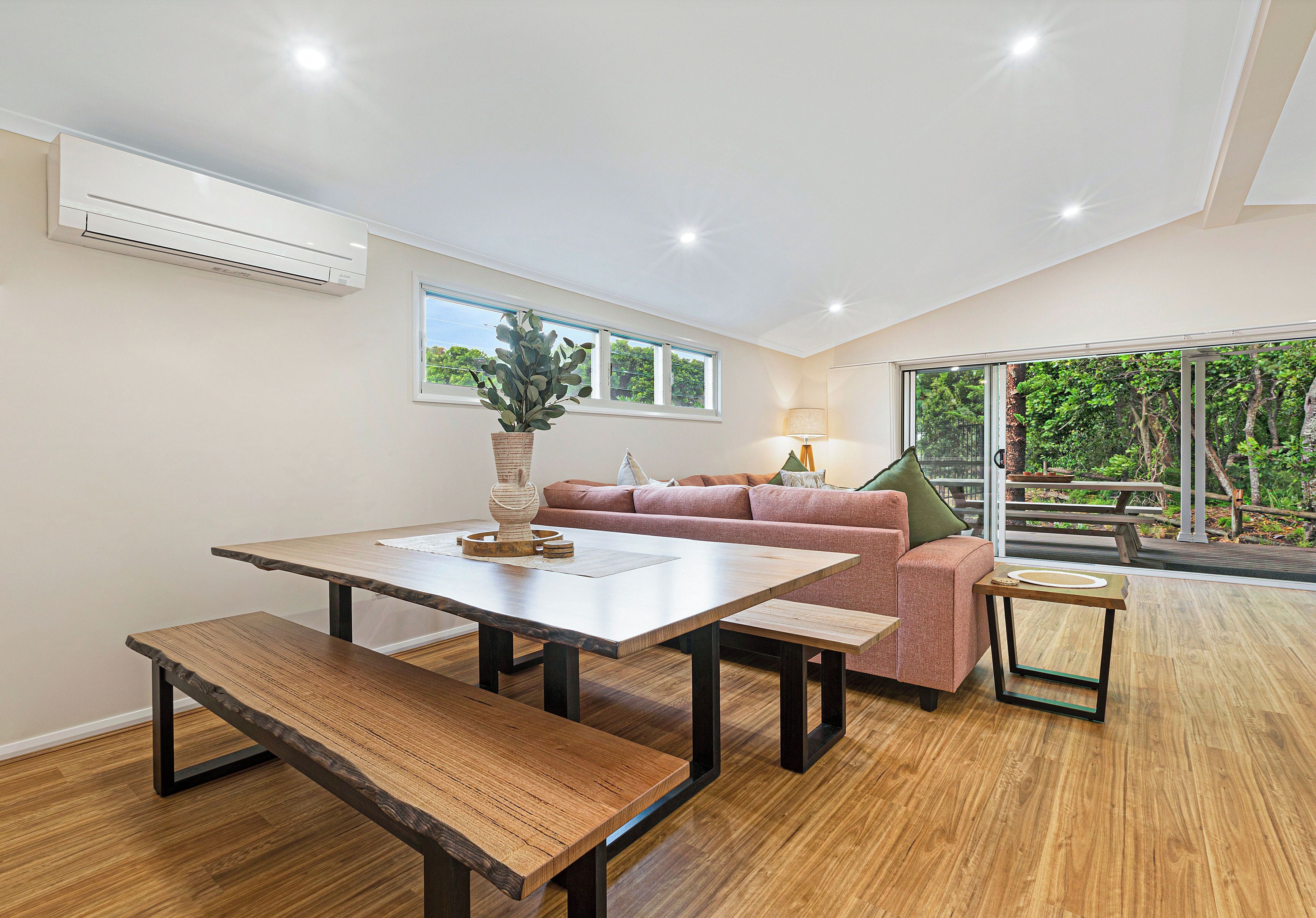 A modern living room with a wooden dining table, benches, a pink sofa, and a small side table.