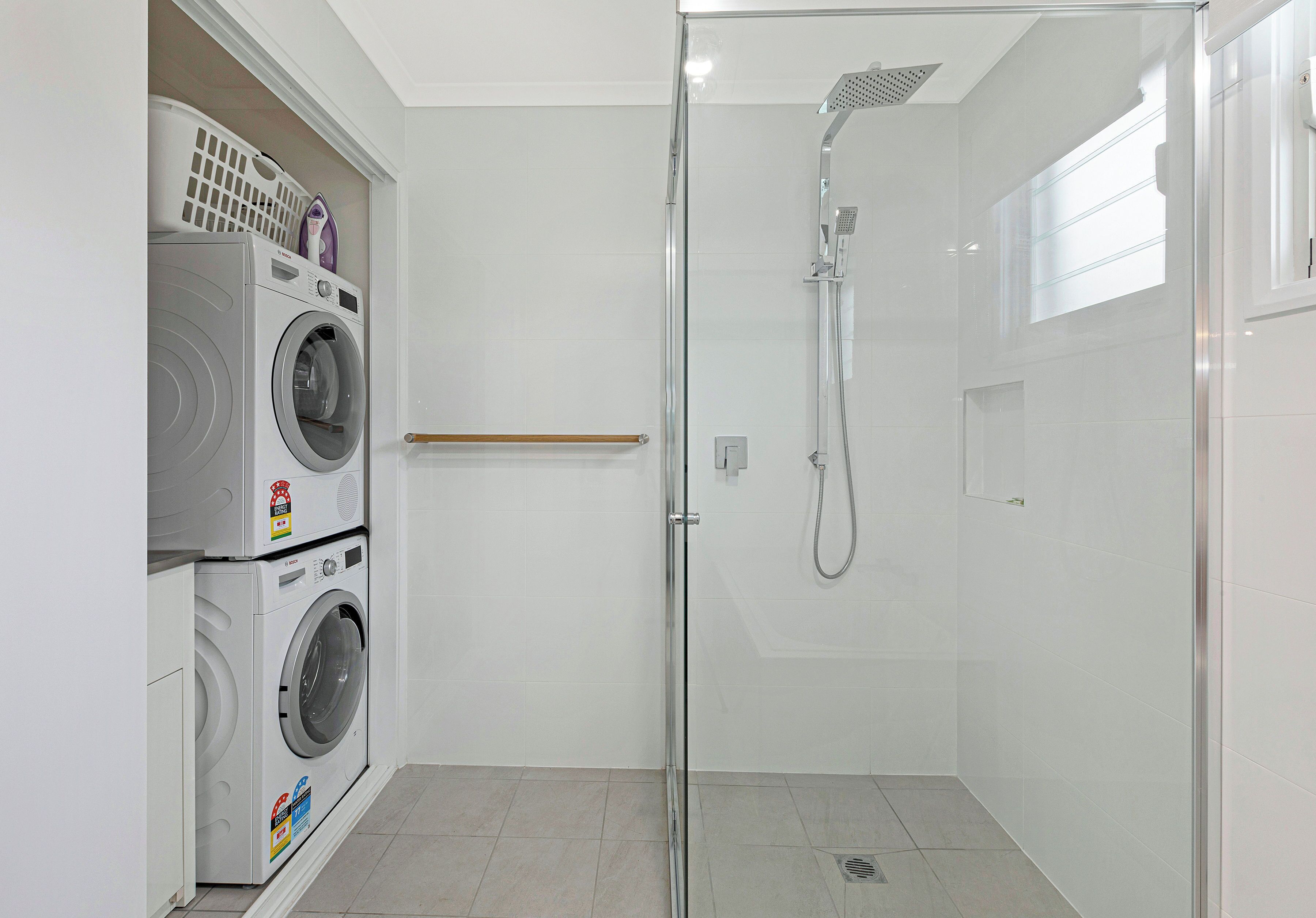 Un bagno compatto con doccia vetro-muraria, lavasciuga affiancata e un piccolo ripiano con cesti per la biancheria.