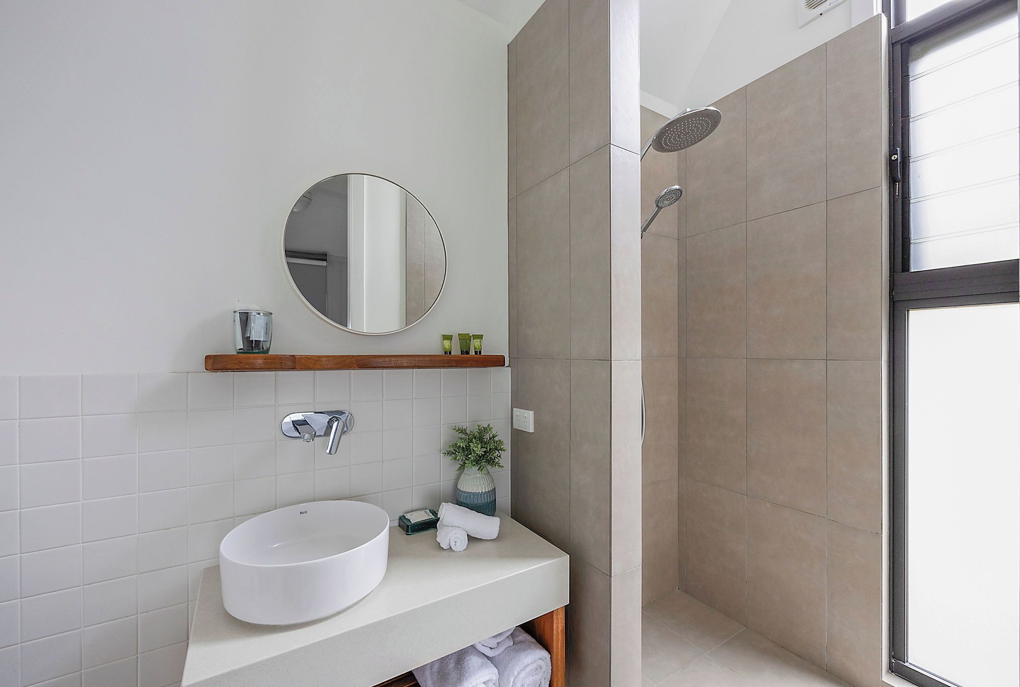 A modern bathroom with a white sink, a round mirror, and a shower area.