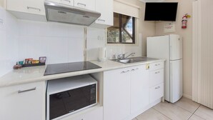 A modern kitchen with white cabinets, a built-in microwave, a stainless steel range hood, a sink, and a refrigerator. - Reflections Red Rock - Holiday Park (Red Rock)