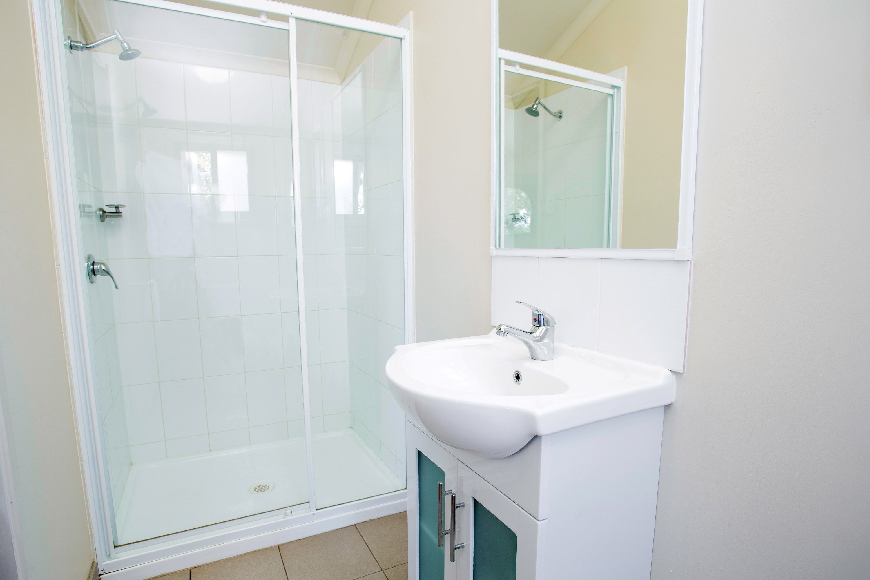 Un baño con ducha de vidrio, un lavabo blanco y un espejo encima.